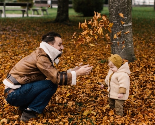 man and baby playing with autumn leaves Thanksgiving