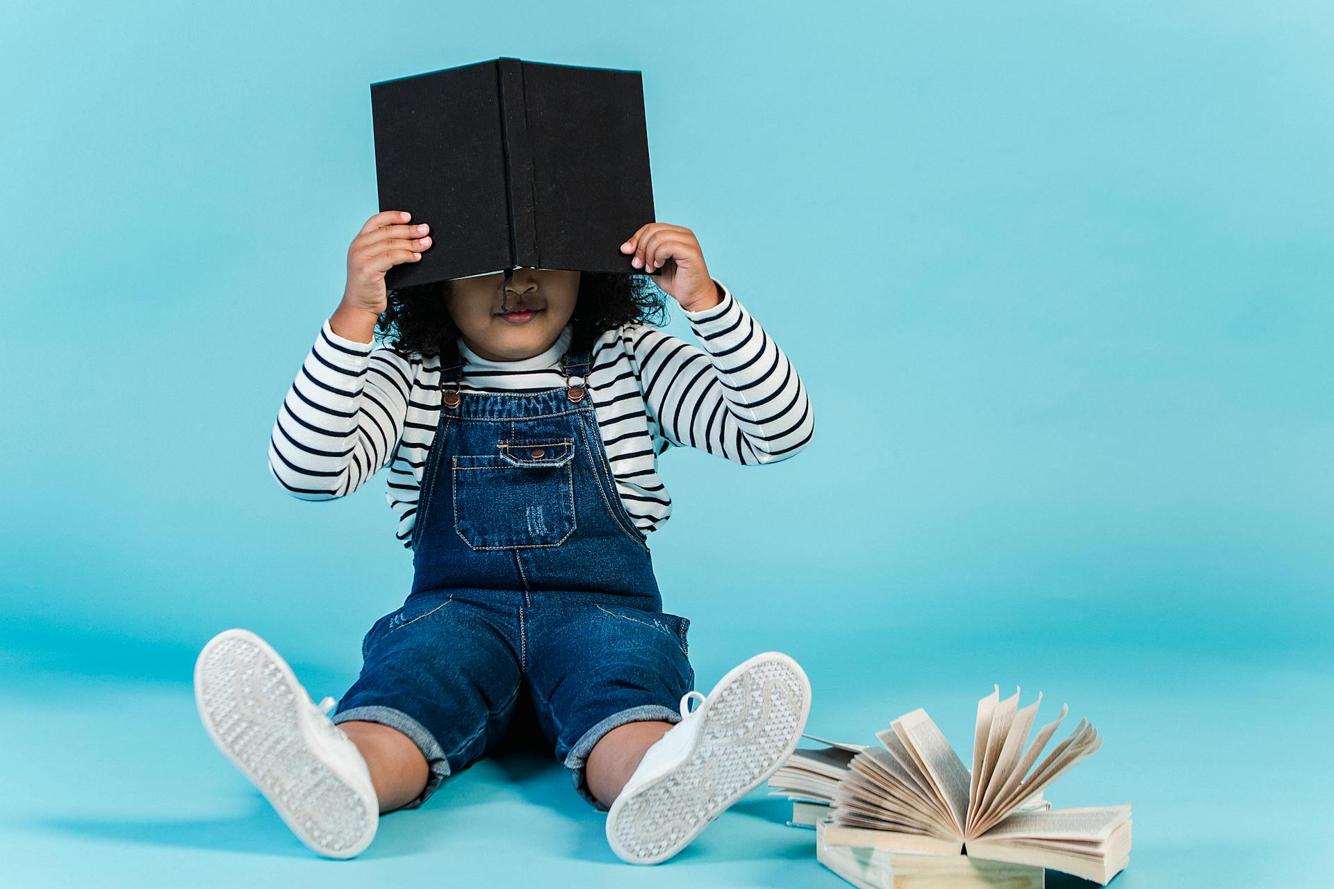 girl sitting on floor with book covering her face