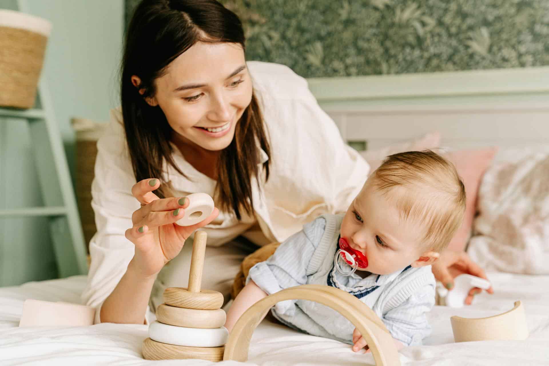 Mother and baby playing with wooden toy in bed