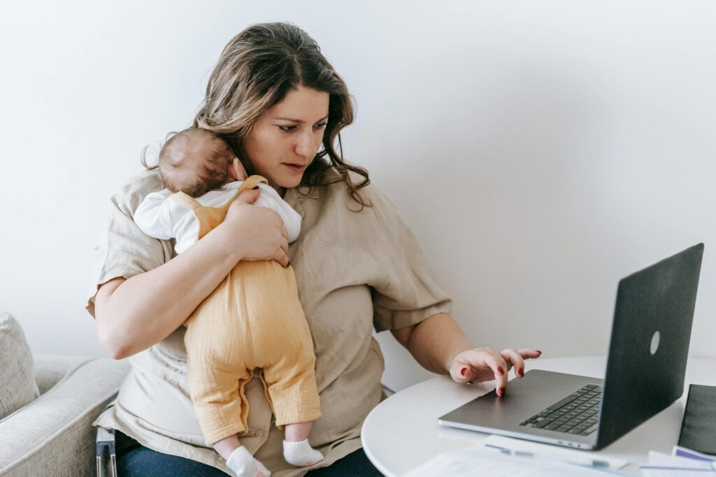 Mother holding her baby while working on a laptop